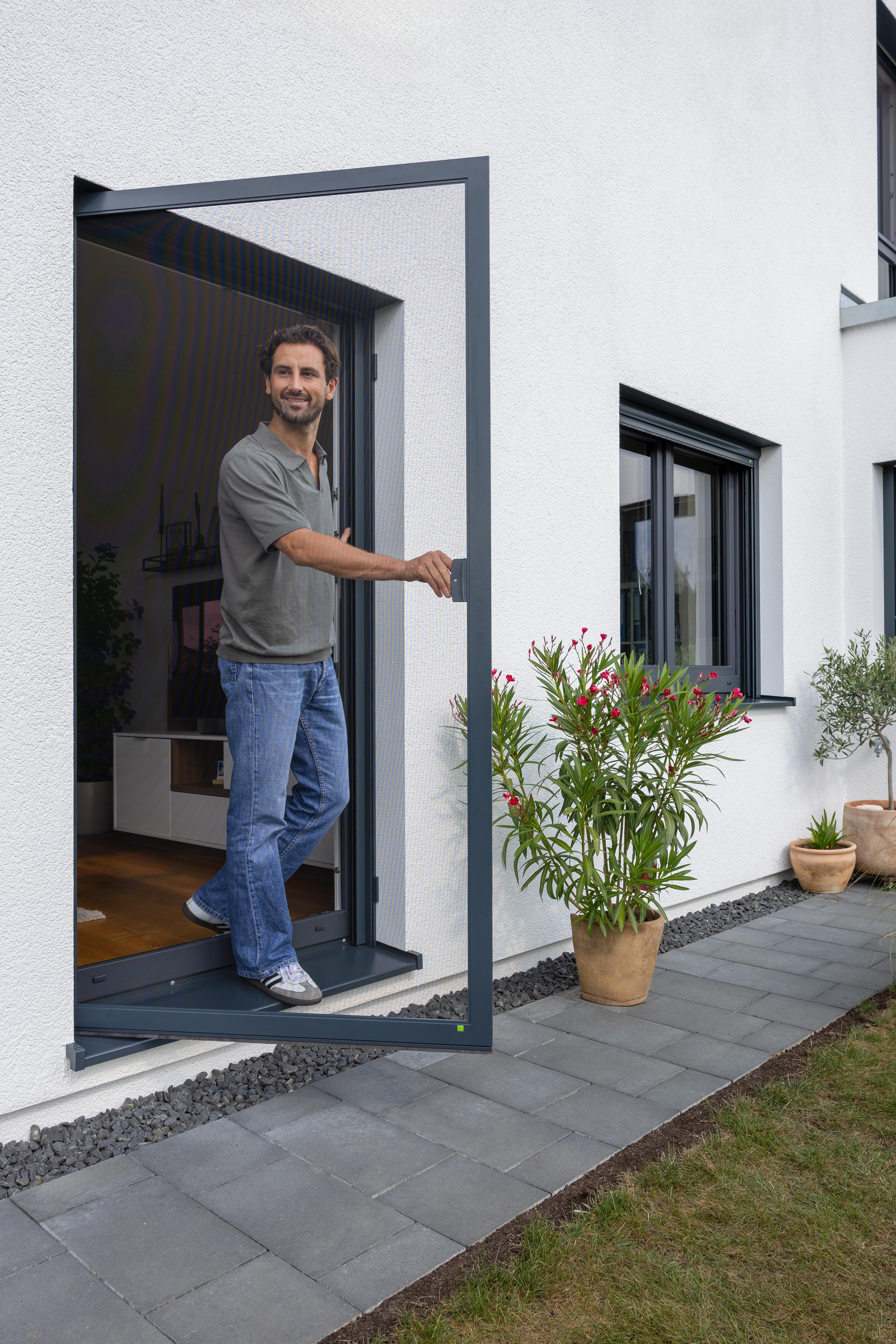 Mann öffnet anthrazitfarbene Insektenschutz-Drehtür aus Aluminium an Terrassentür
