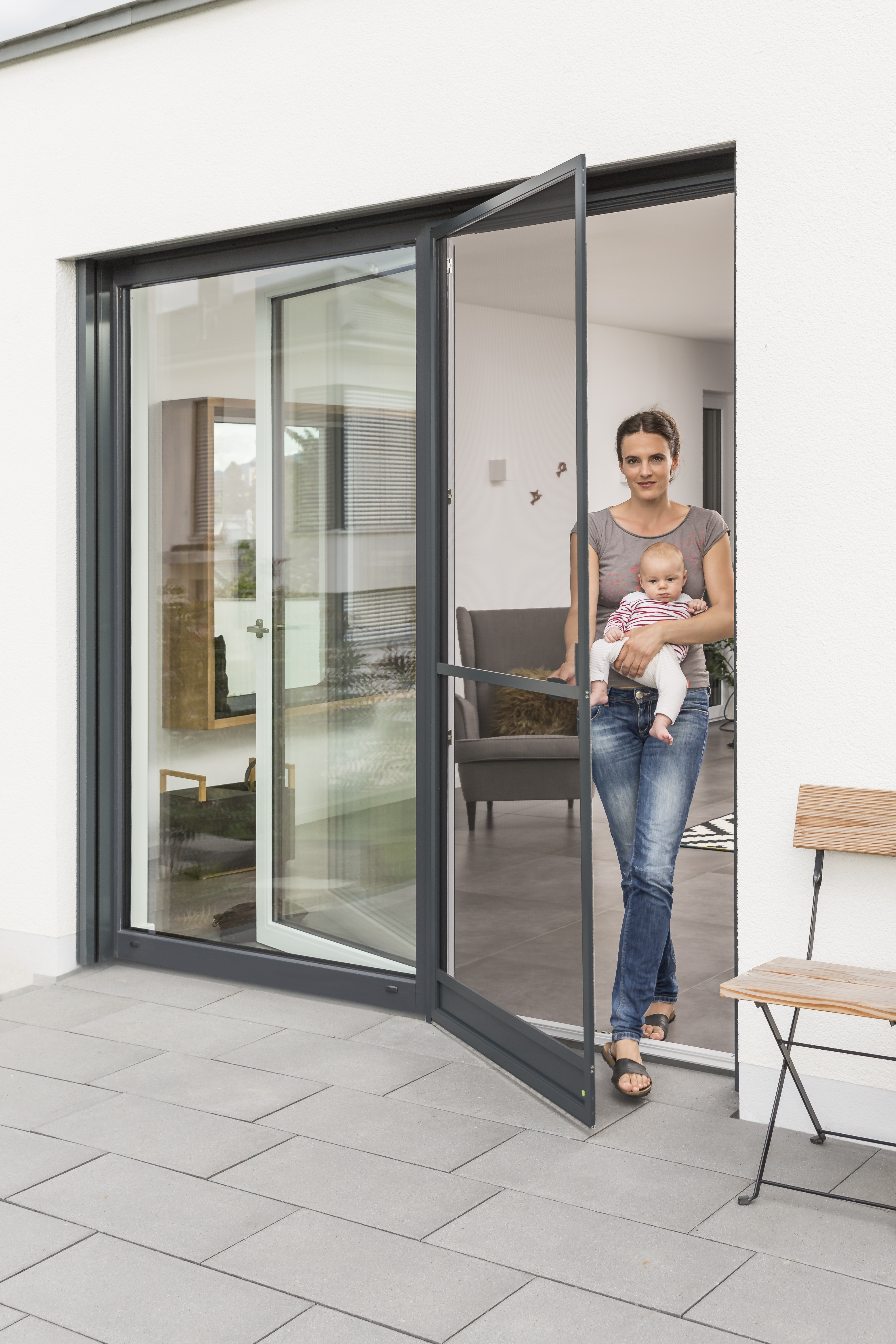 Frau mit Baby steht in offener Insektenschutz-Drehtür vor Terrassentür