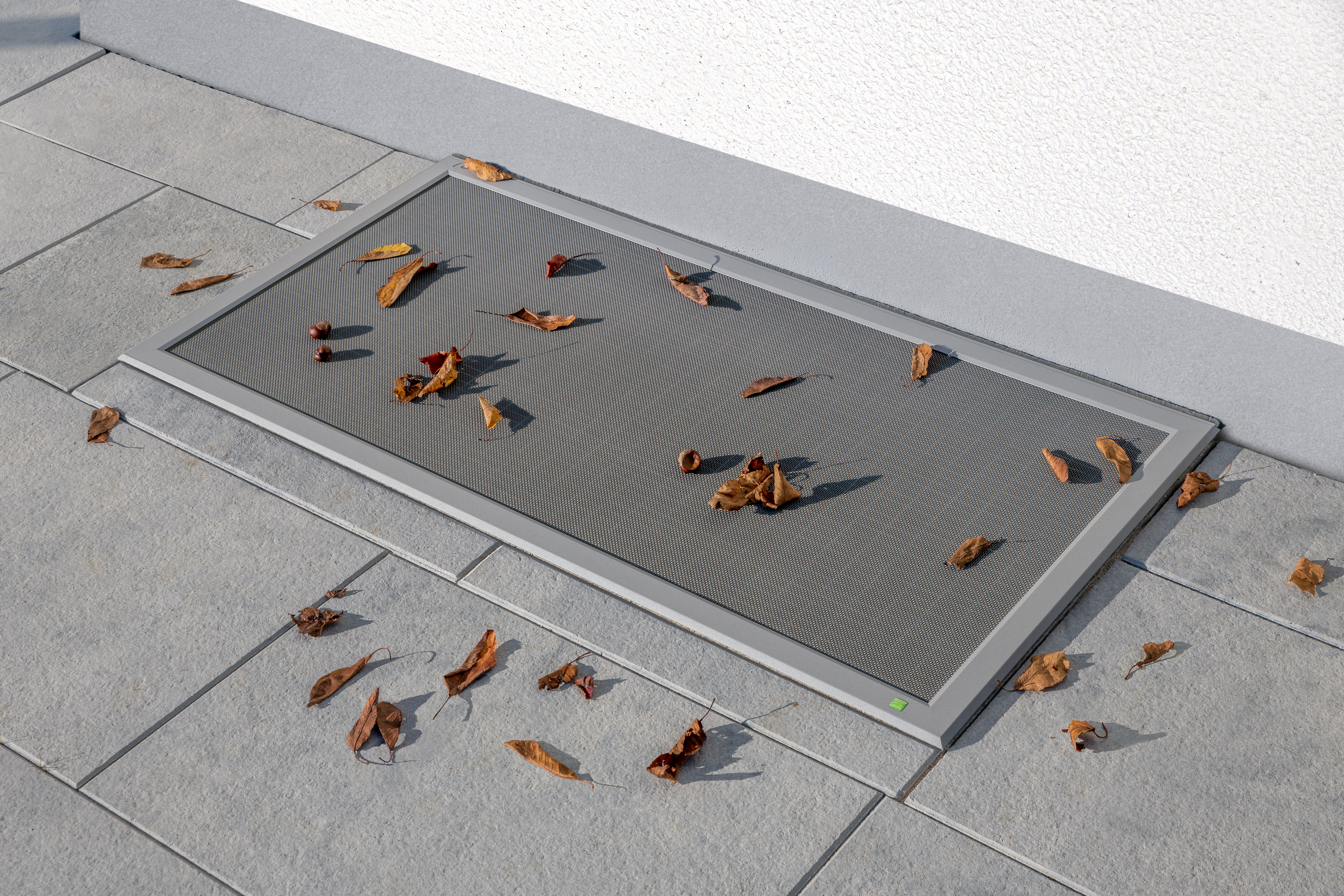 Kellerschachtabdeckung mit stabilem Aluminiumrahmen und feinmaschigem Gitter, Laub liegt auf der Oberfläche