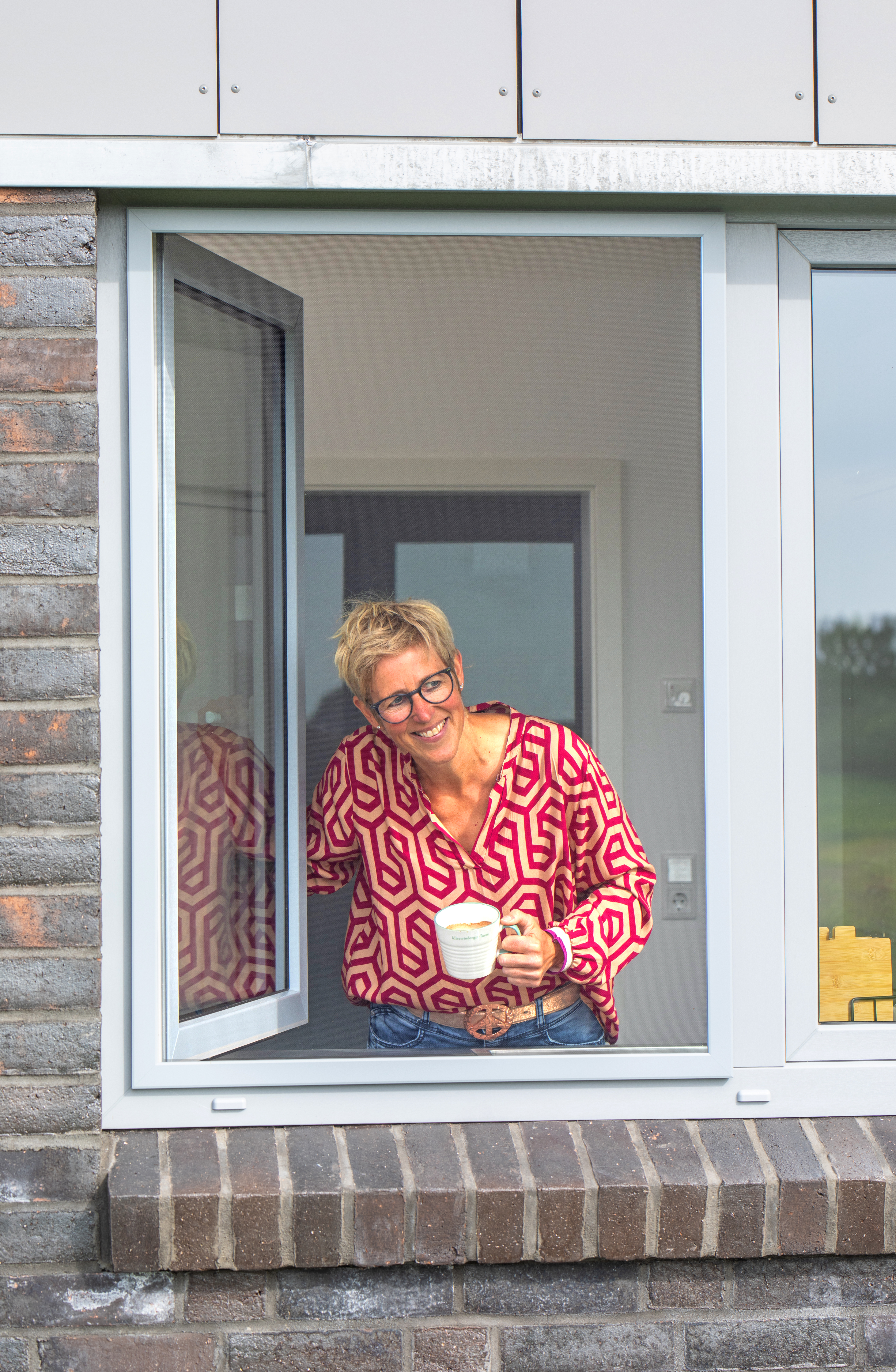 Frau schaut durch ein geöffnetes Fenster mit Insektenschutz-Spannrahmen – freie Sicht bei maximalem Schutz.