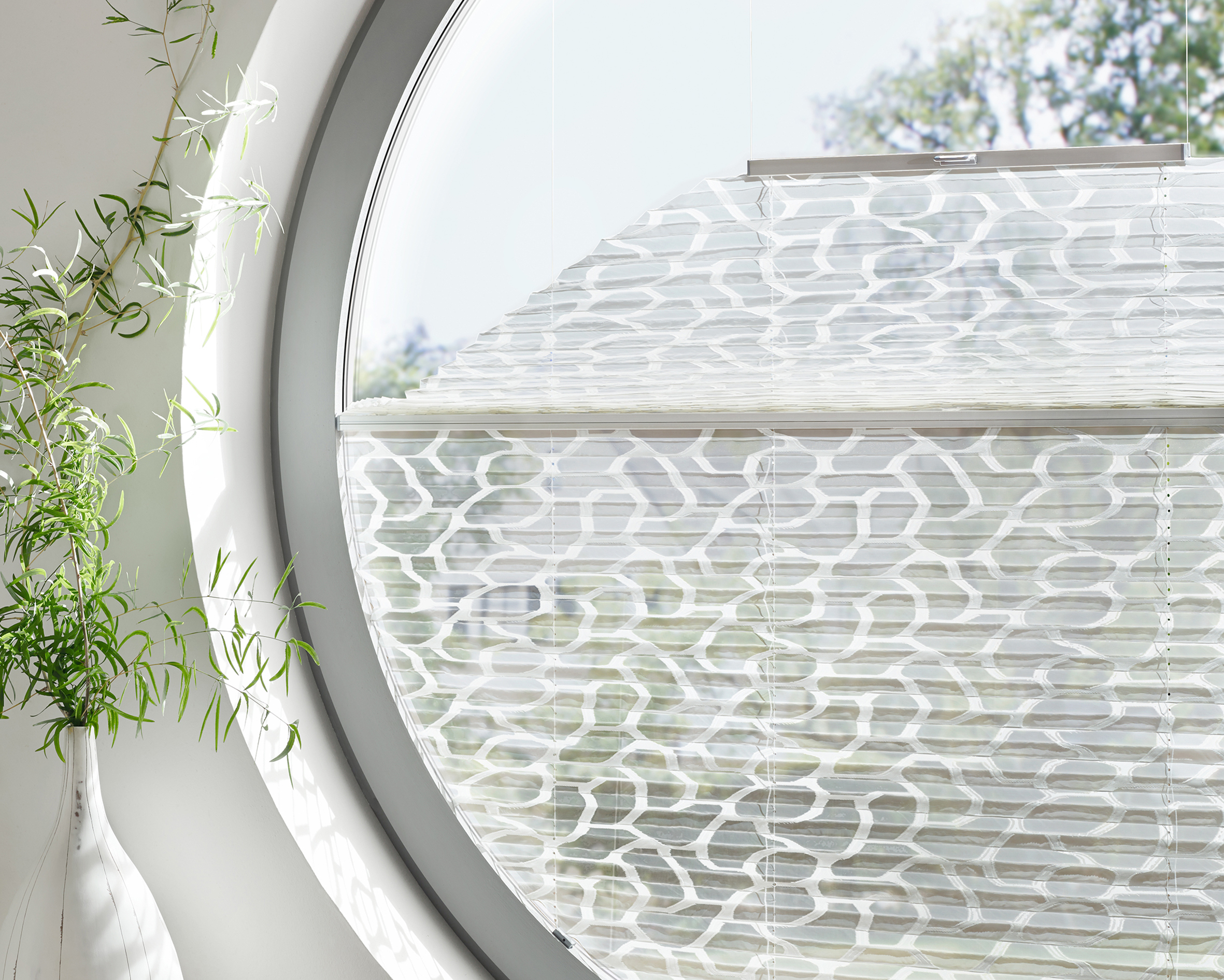 Weißes Plissee mit hell gemustertem Stoff in rundem Fenster. - Schmidt Insektenschutzrahmen GmbH