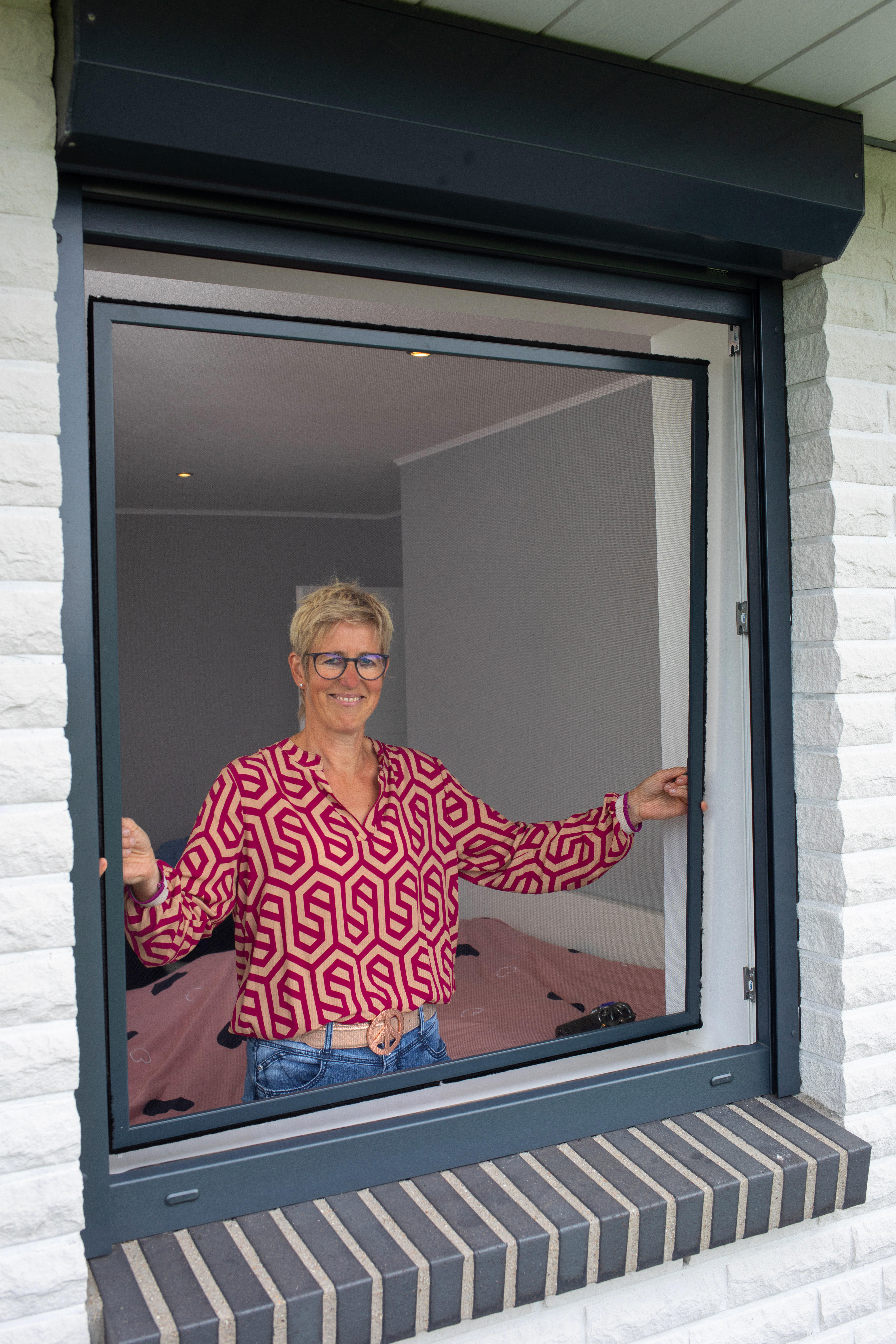 Lächelnde Frau setzt Insektenschutz-Spannrahmen ein bei Fenster mit Außenrollladen