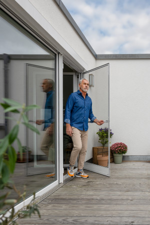 Mann öffnet weiße Insektenschutz-Drehtür an Balkontür – barrierefreier Übergang
