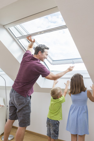 Mann bedient Insektenschutz-Rollo am Dachfenster – ideal für schräge Fensterflächen